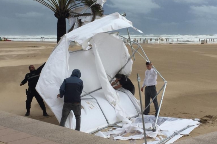 Las fuertes rachas de viento arrastran un toldo en la playa de Gandia